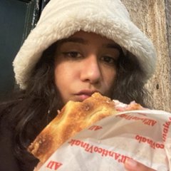 Sana in a fuzzy bucket hat, mid-bite of a giant sandwich